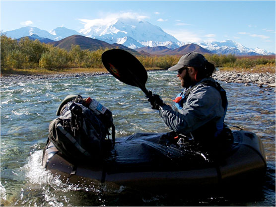 a man sitting in a small raft on a river, with a huge snowy mountain in the distance a man sitting in a small raft on a river, with a huge snowy mountain in the distance