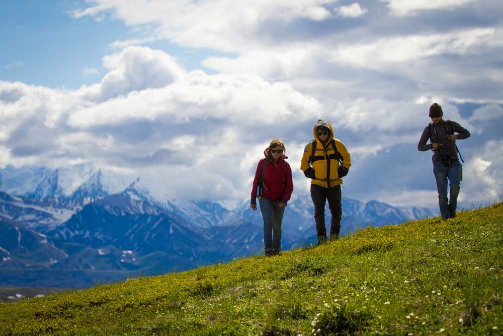 three people walking on a green hillside