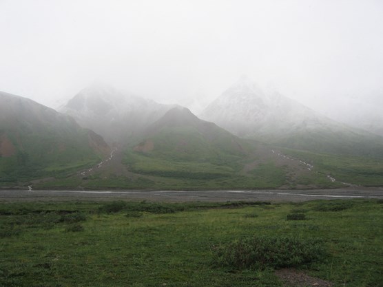 a green plain with mountains in the distance mostly shrouded in gray mist and rain
