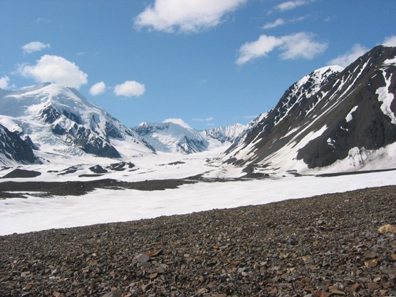snow-covered mountains looming over a gravel and snow-covered mountain pass