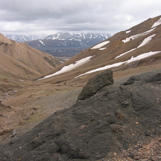 looking downhill from a rocky mountainside dotted with snow
