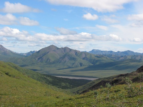 looking down a hillside to a river valley with mountains on the far side