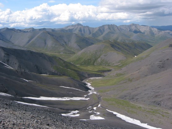 a rocky, snow-dotted slope leading down to a creek, mountains in the distance