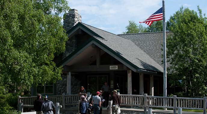 a brown-colored building amid trees, with several people in front of it a brown-colored building amid trees, with several people in front of it