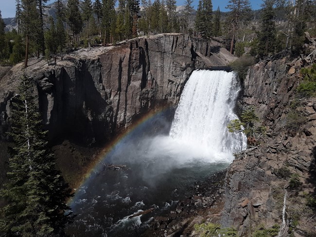 A wide river drops 100-foot as a waterfall with a rainbow in the mist