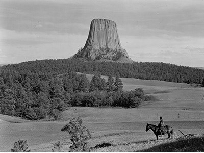 A man on horseback near the foreground with Devils Tower in the background.