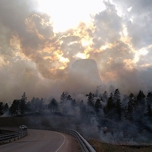 A rock monolith obscured by smoke with fire in the foreground.