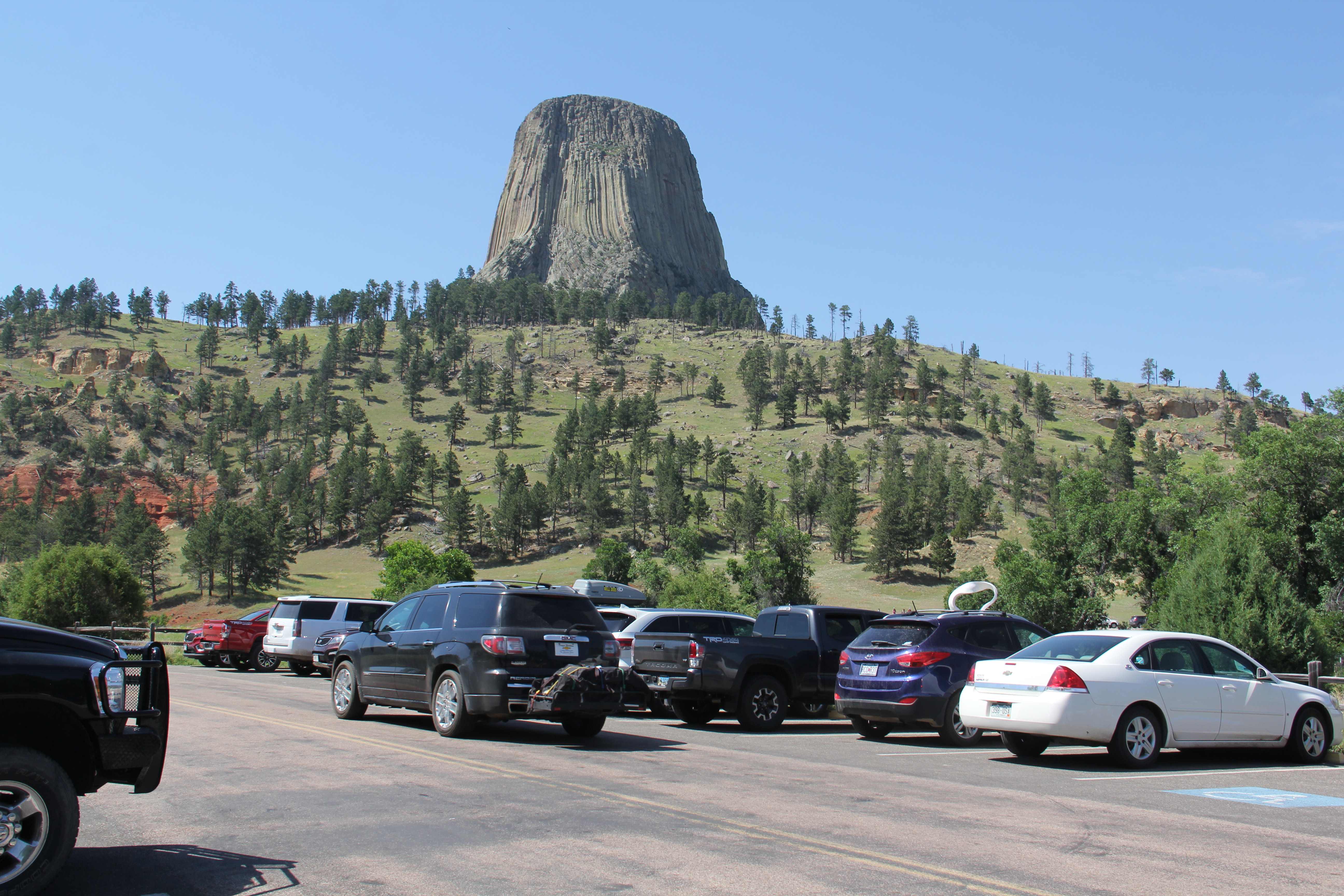 A car searches for parking in a busy lot with Devils Tower in the background