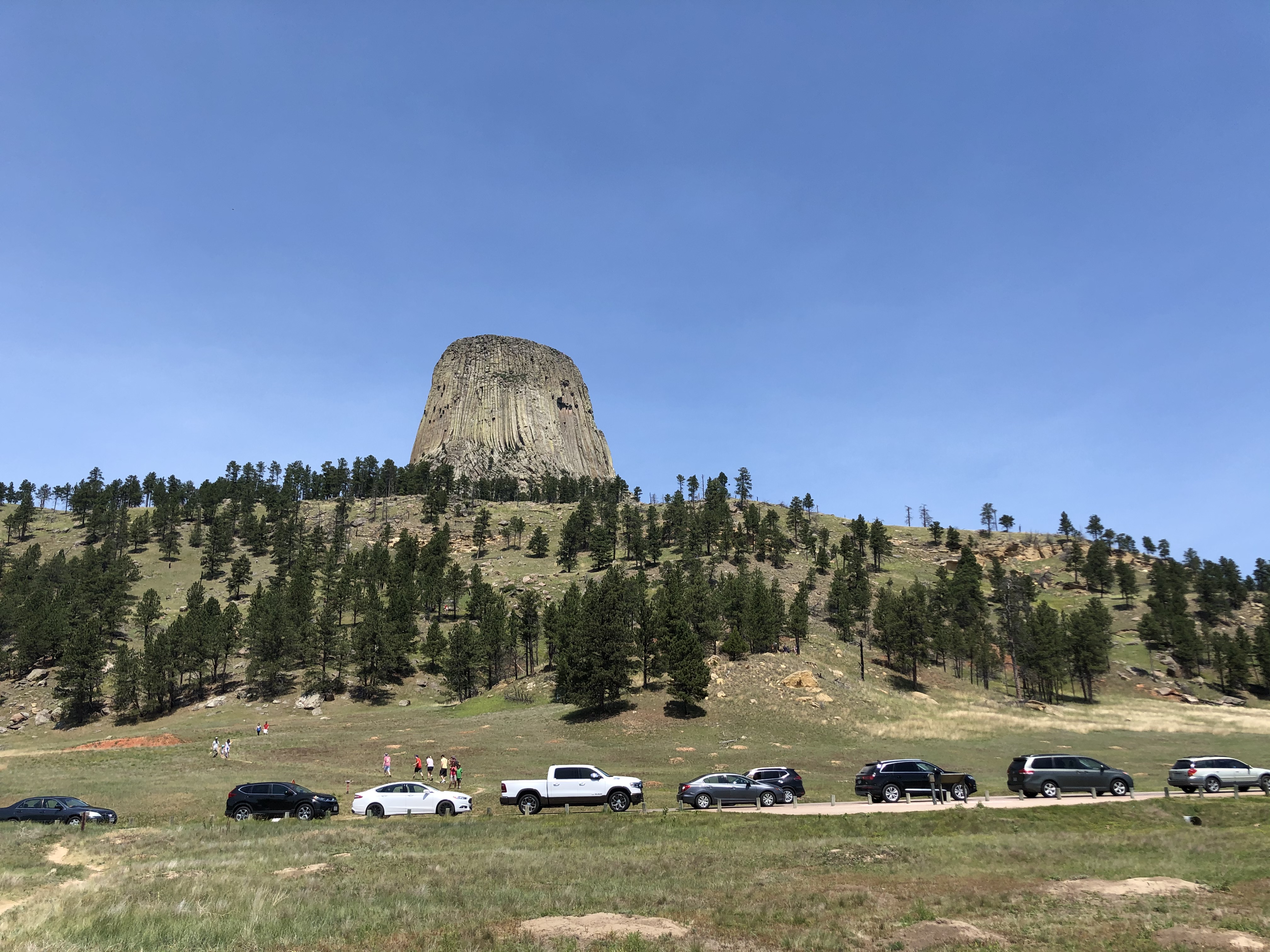 busy September road a line of cars in pullouts along the roadside with people hiking on the ridgeline beyond and Devils Tower in the background