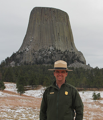 A man standing in front of a giant rock monolith.