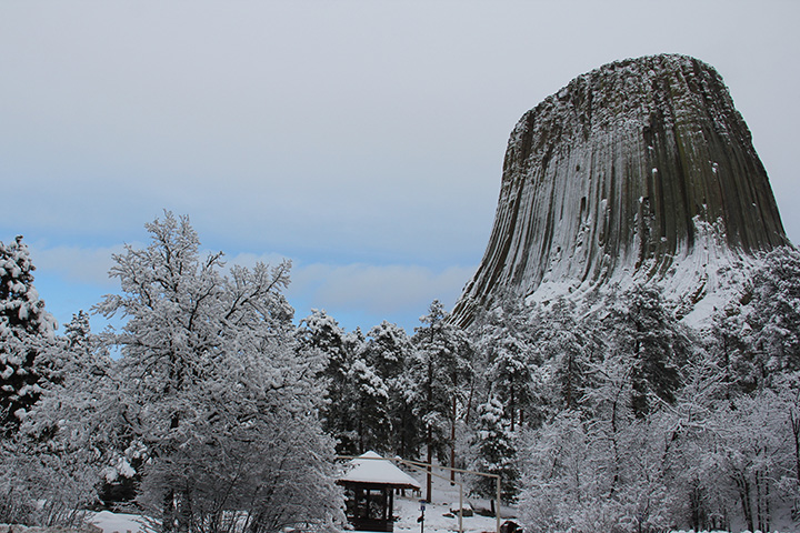 A snowy scene with trees, a small kiosk, and giant rock monolith in background