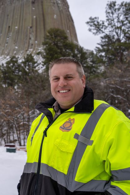 Man Standing in front of Devils Tower wearing blaze green jacket on cloudy winter day