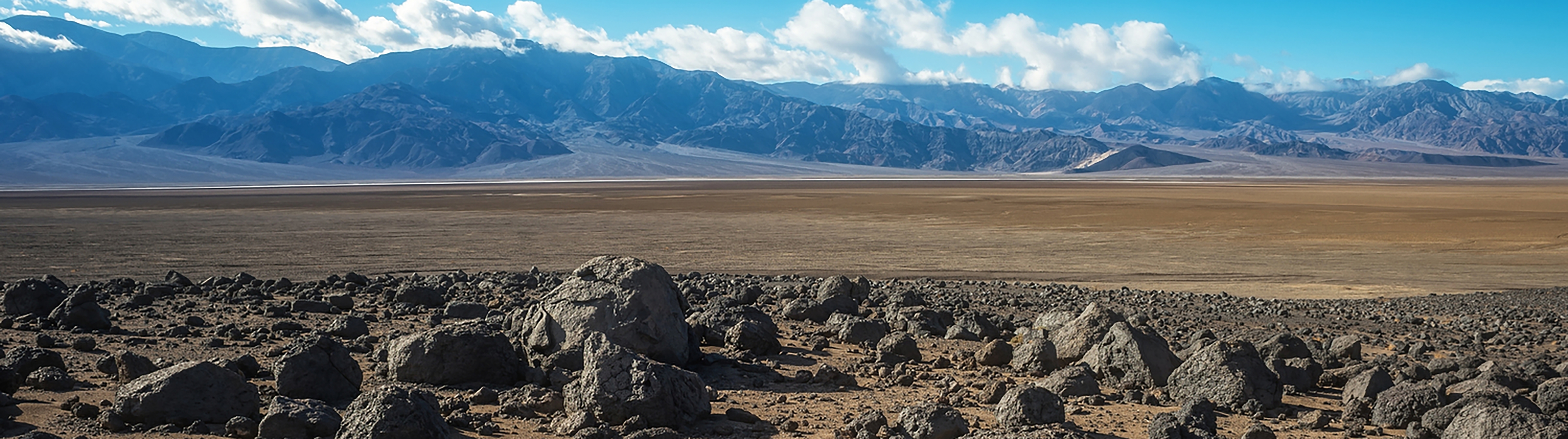 The foreground is strewn with dark, jagged rocks, creating a stark contrast with the smooth, sandy expanse in the middle of the scene.