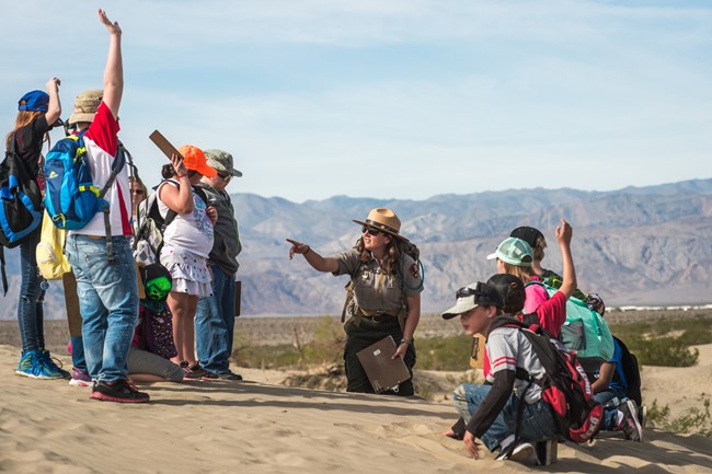 Students raise their hands around a park ranger giving an educational program at the sand dunes