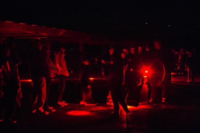 People stand around a telescope at night.