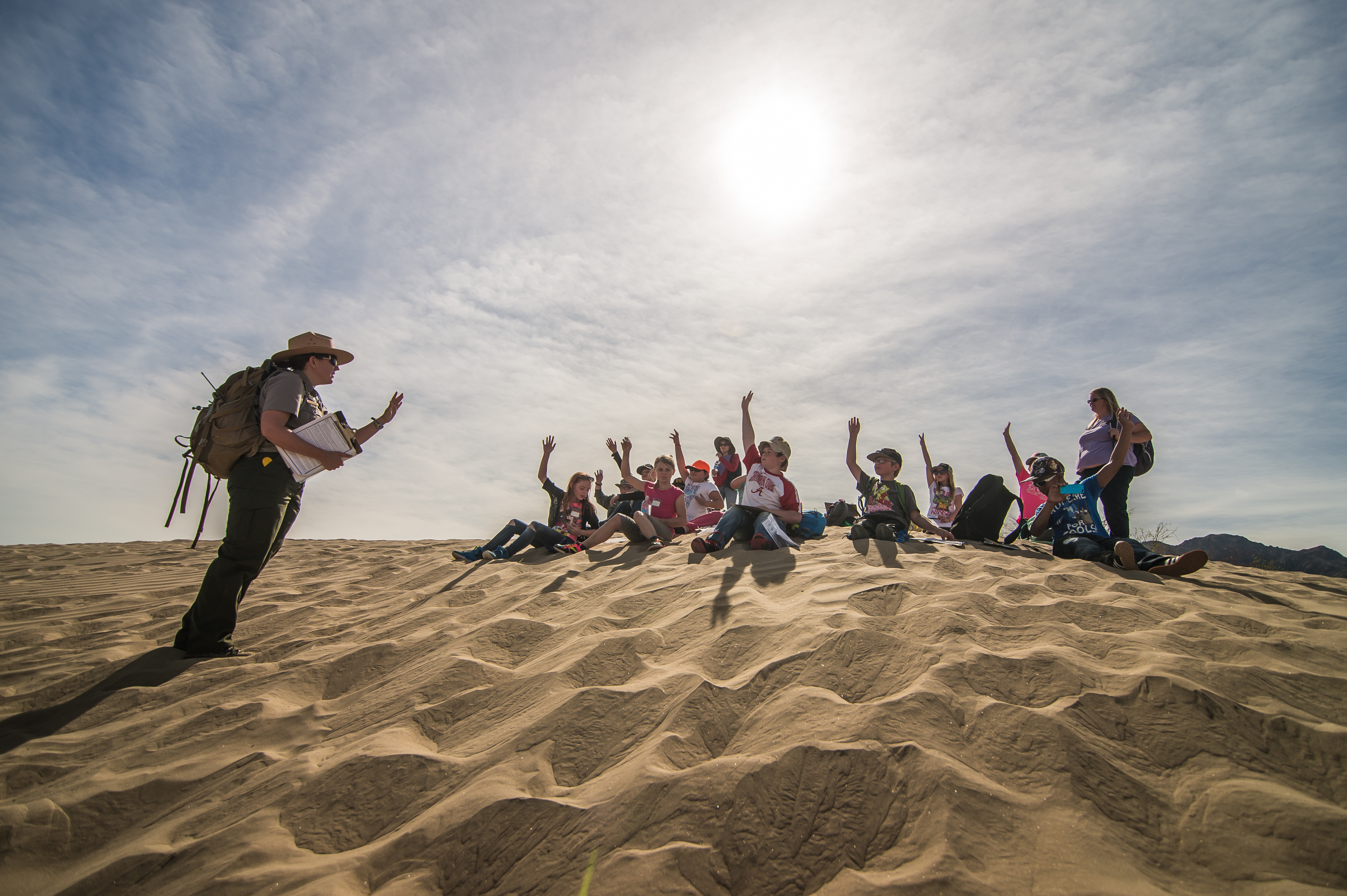 Students sit in front of a ranger on the sand dunes.