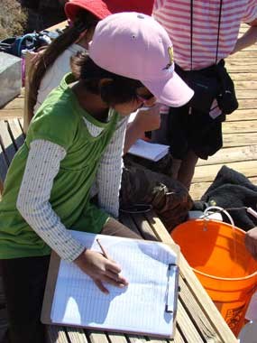 A student writes on a clipboard while looking into a bucket.
