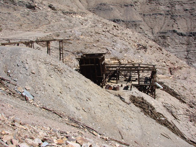 Keane Wonder Mine Upper Tramway Terminal Brown-hued desert hillside with a large, house-sized wooden platform and shelter in the center.