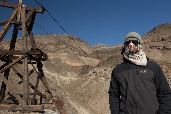 A hiker stands under a wooden tram tower in the desert.