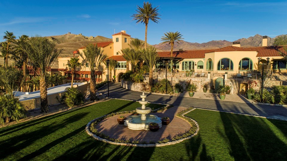 Photograph of the Inn, showing a lawn and fountain in the foreground, and the historic mustard-colored Inn in the background.