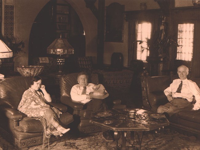 three people seated in a lavishly furnished house
