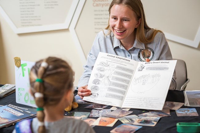 A ranger points to drawings in a Junior Ranger book with a young kid in the foreground.