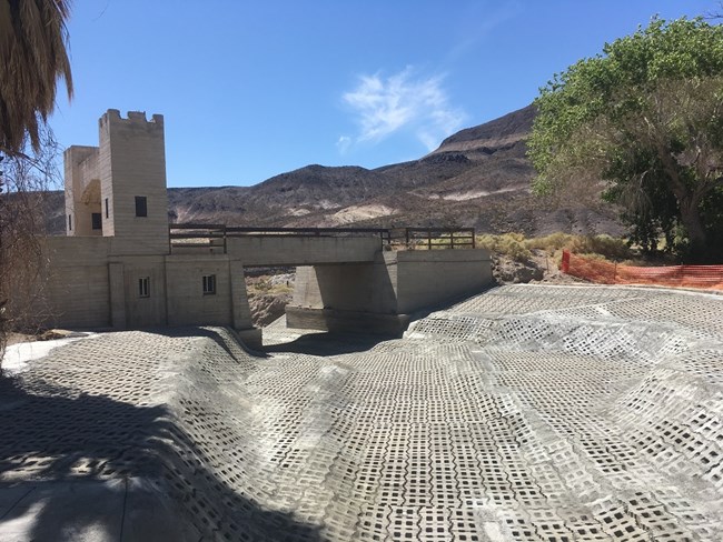 The historic concrete bridge is seen in the background, viewed from the east side. In the foreground is an extensive area covered by articulated concrete blocks.