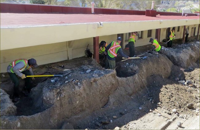 people in safety vests digging mud from around a building