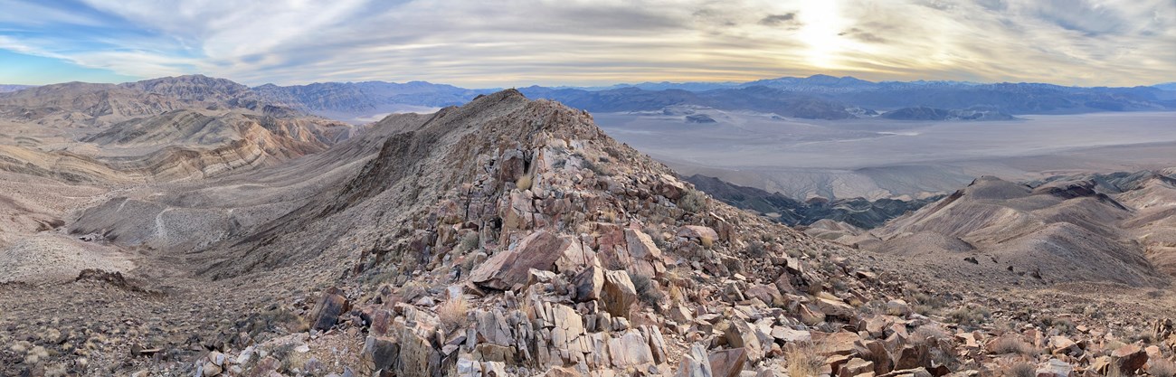 View from a bare rocky ridge of desert mountains with a desert valley below.