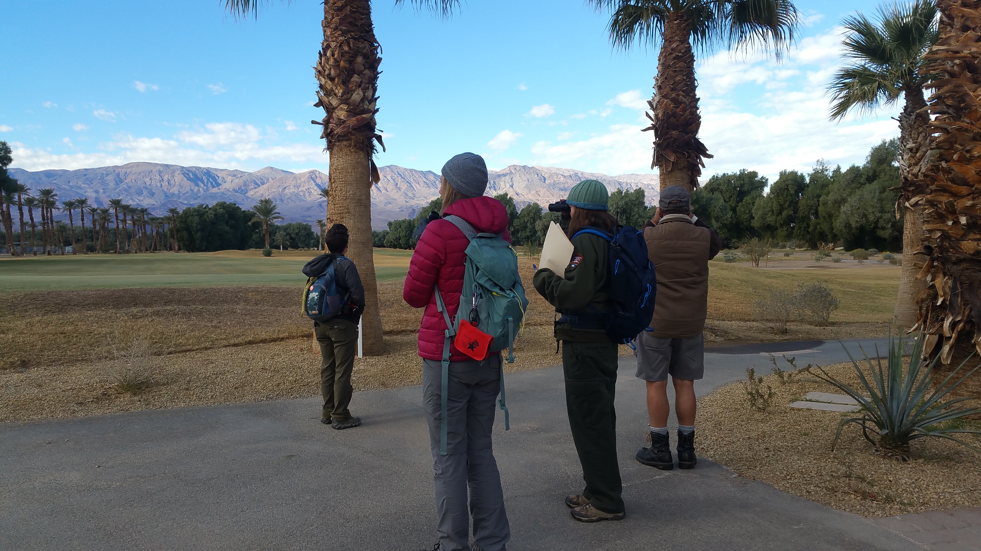 A NPS employee and park visitors stand looking for birds at Furnace Creek Golf Course.
