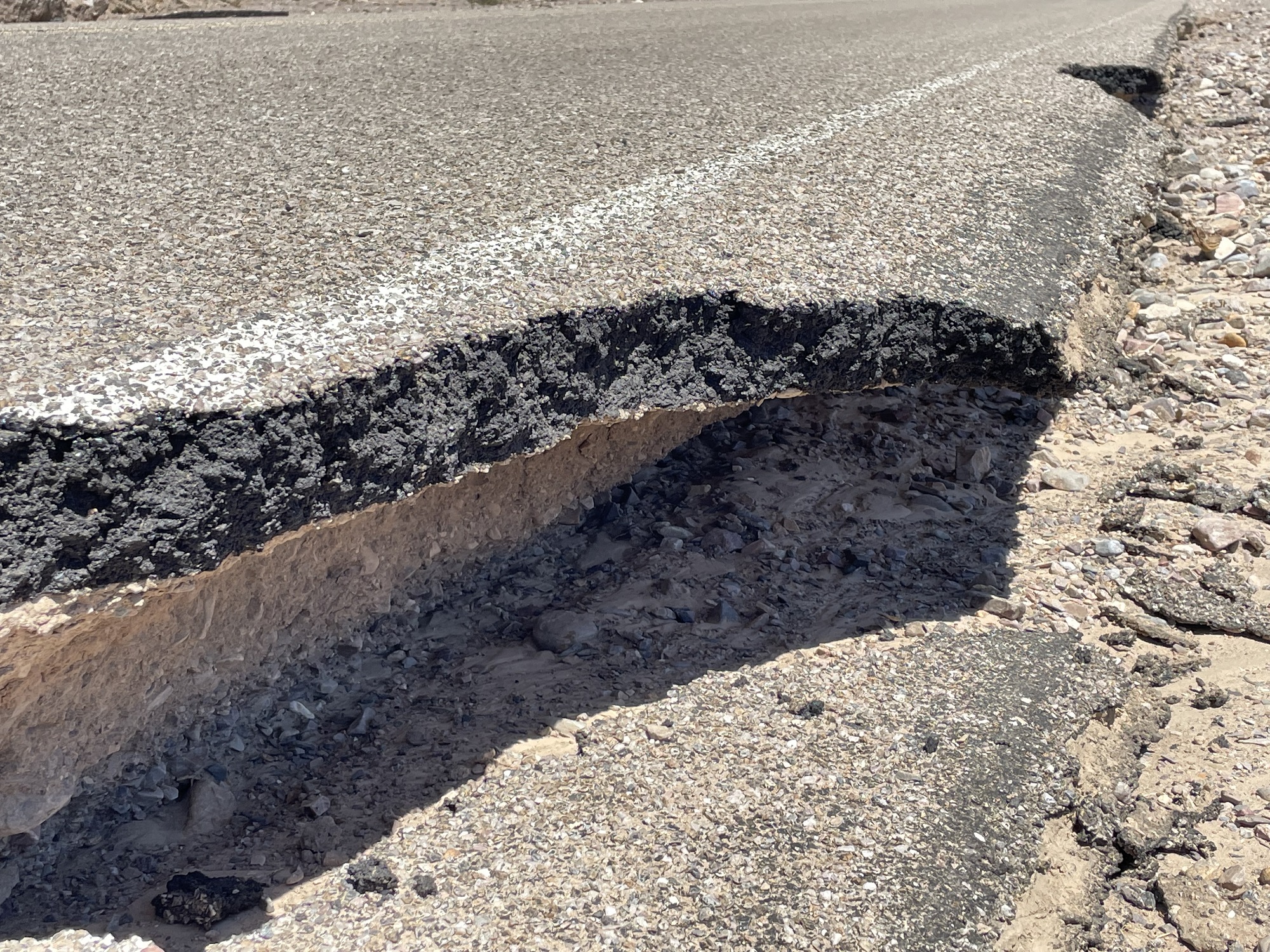 Close-up view of the edge of a paved road, showing that the ground under the pavement edge has been washed away.