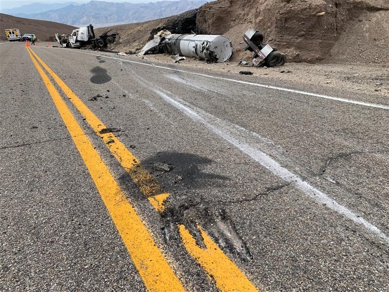 Wrecked tractor trailer on the side of a paved road.