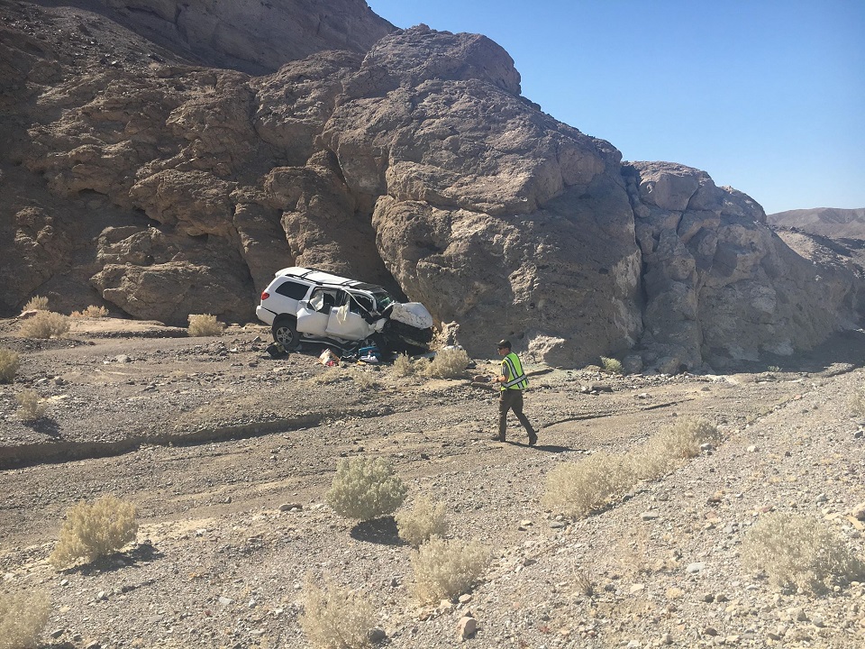 A park ranger walks towards the scene of the traffic collision. No road is in sight and the white SUV appears to have smashed into the rock wall at high speed.