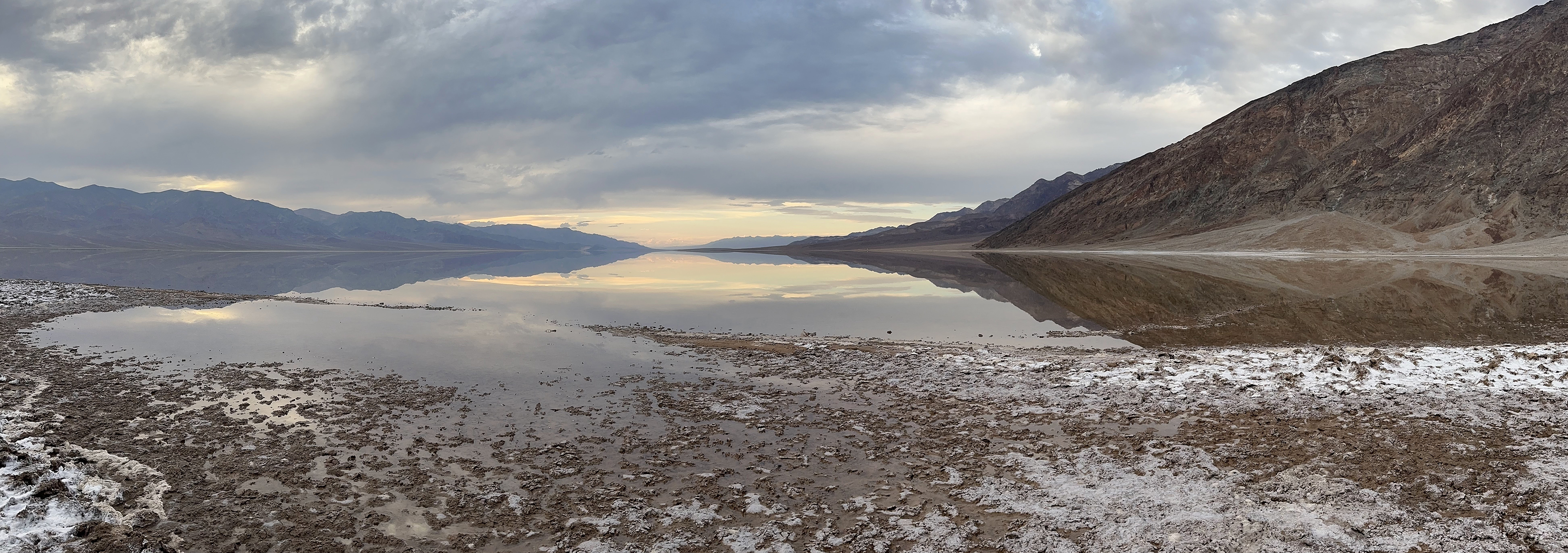 Desert mountain landscape surrounding a salty flat valley with a thin layer of water on the valley flood reflecting the landscape.