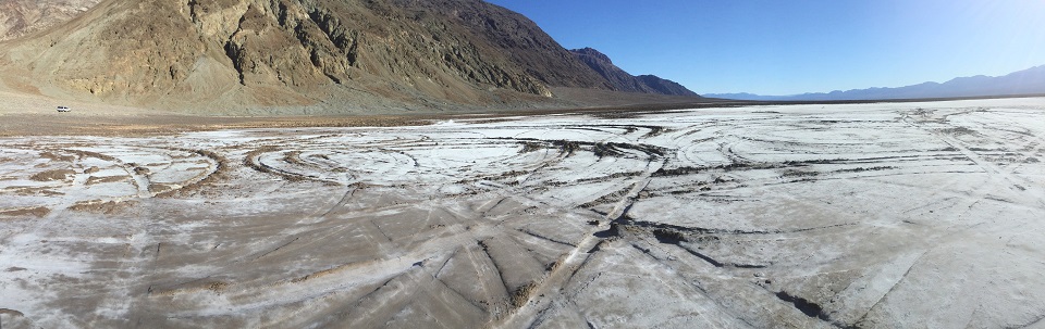 Ruts in the white salt pan are visible in the foreground from multiple vehicles. Mountains are in the background.