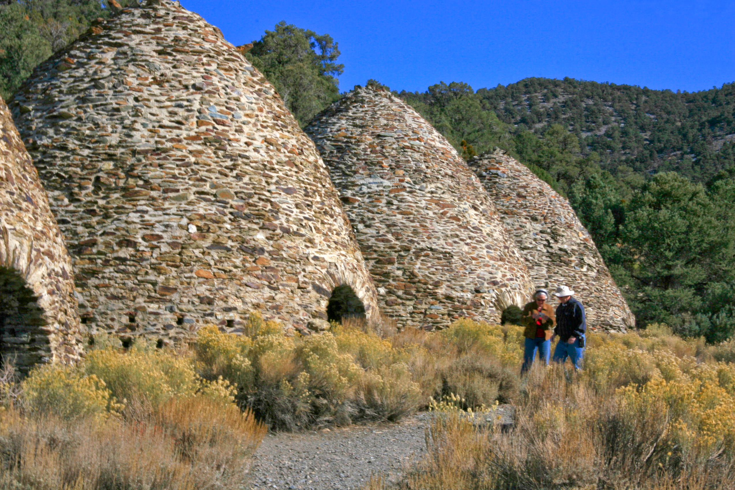 Two people stand near four large stone structures shaped like bee hives.