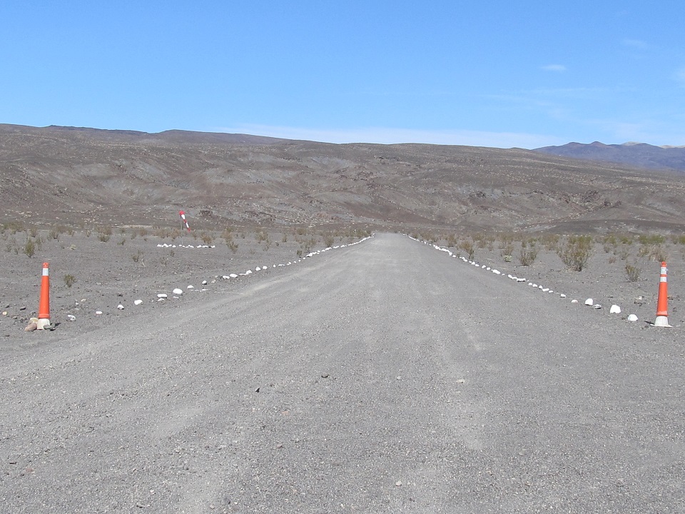 Commonly known as the "Chicken Strip", Saline Valley's airfield is an unpaved runway surrounded by low desert shrubs with a small hill in the background.