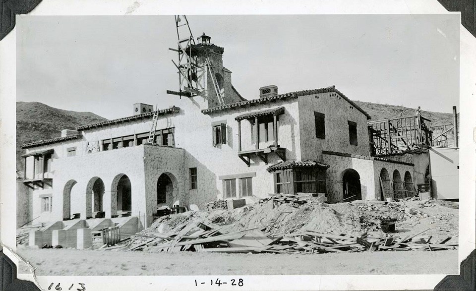 Black and white photo of a two-story building with ornate porches, and a roof-top tower. The building has a stucco finish. There are some ladders and scaffolding in place. "1613" and "1-14-28" are hand-written on the bottom.