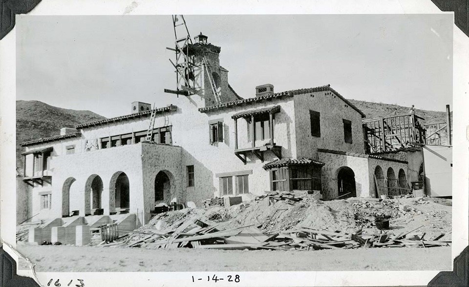DEVA 40518 Black and white photo of a two-story building with ornate porches, and a roof-top tower. The building has a stucco finish. There are some ladders and scaffolding in place. "1613" and "1-14-28" are hand-written on the bottom.
