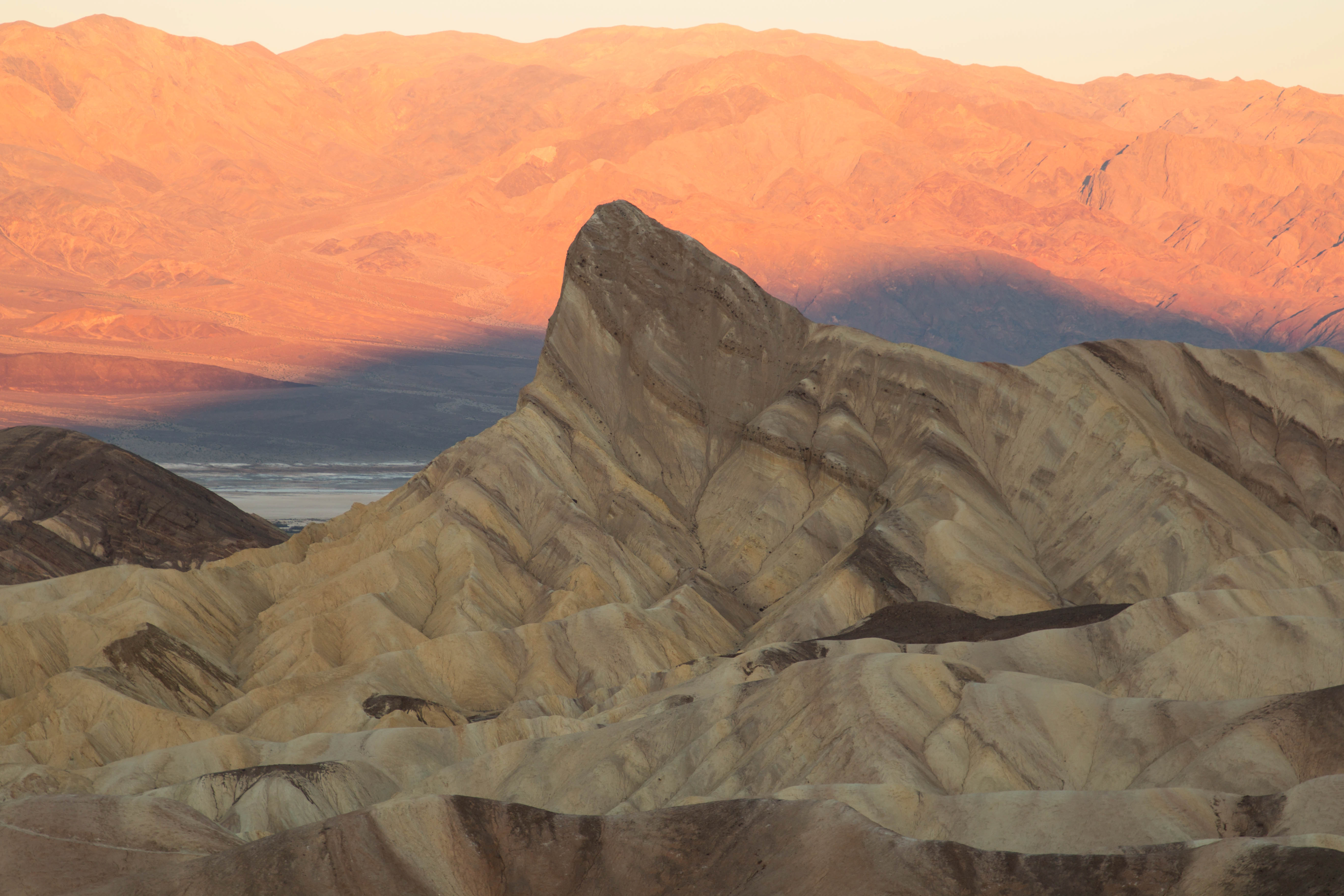 badlands with a prominent hill and sunrise light turning distant mountains pink