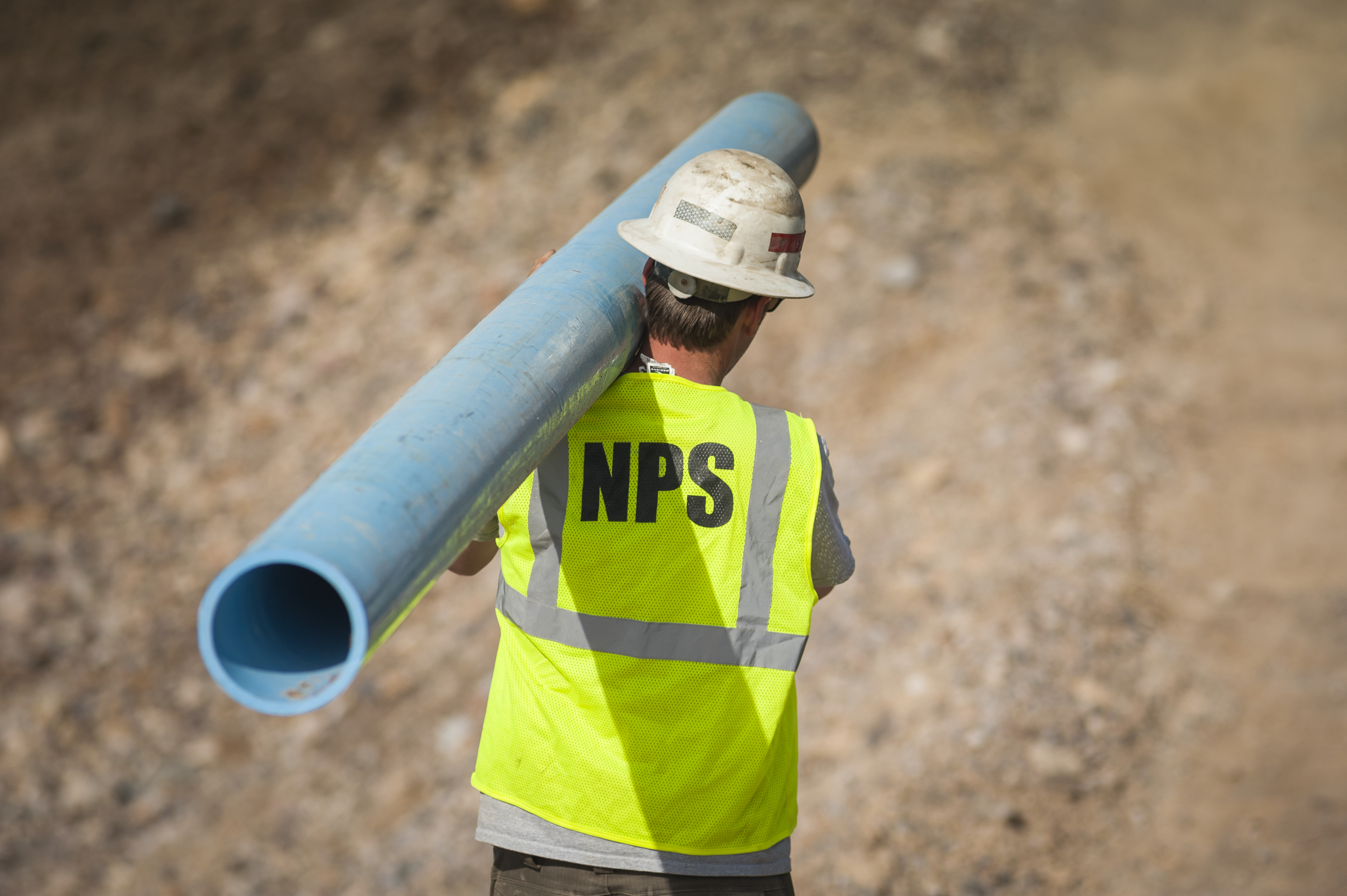 A National Park Service employee carries a replacement pipe segment.