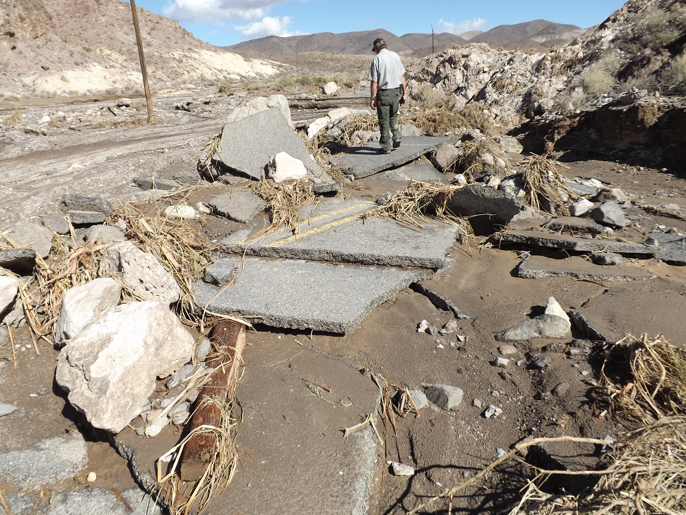 a park employee inspects the broken pavement of a road after a flood