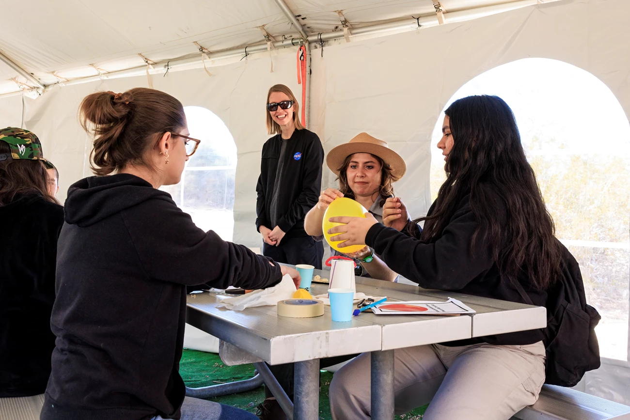 People sit at a picnic table doing something to a yellow balloon.