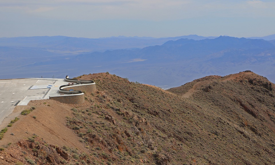 This photograph of Dantes View was taken from the trail to Dantes Peak, looking slightly down on the viewpoint. The concrete platform is bounded by a low block wall topped by a railing.