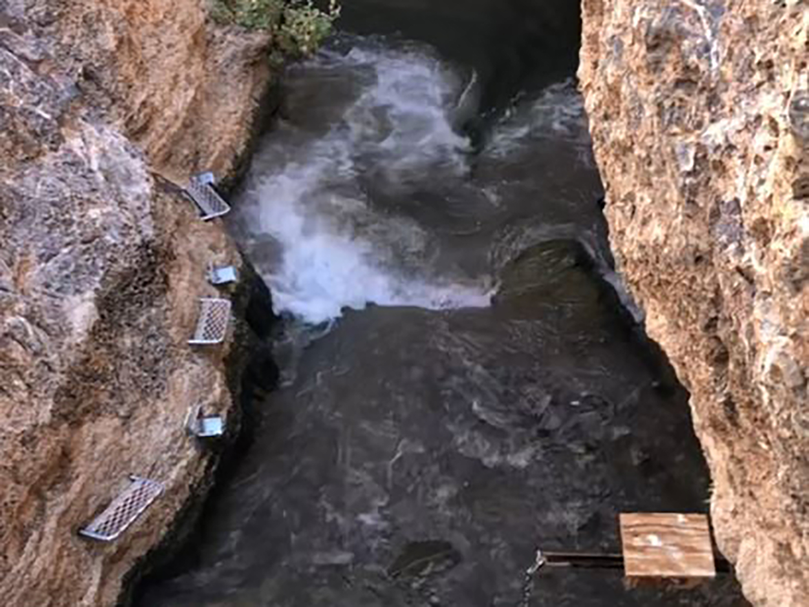 A slightly-blurring screen shot of a video shows a wave between tan rock walls.