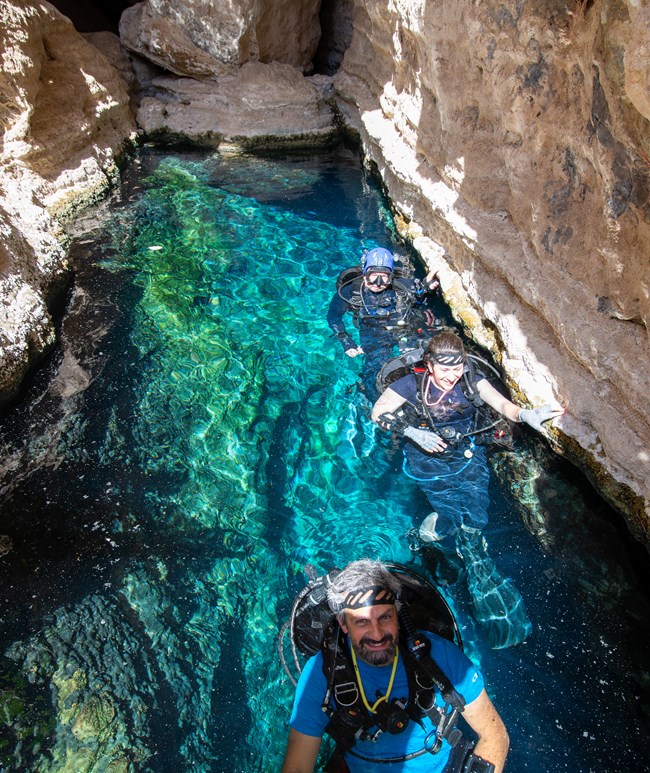 scuba divers in bright blue water in a narrow canyon