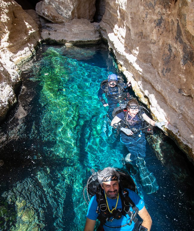 Devils hole dive team scuba divers in bright blue water in a narrow canyon
