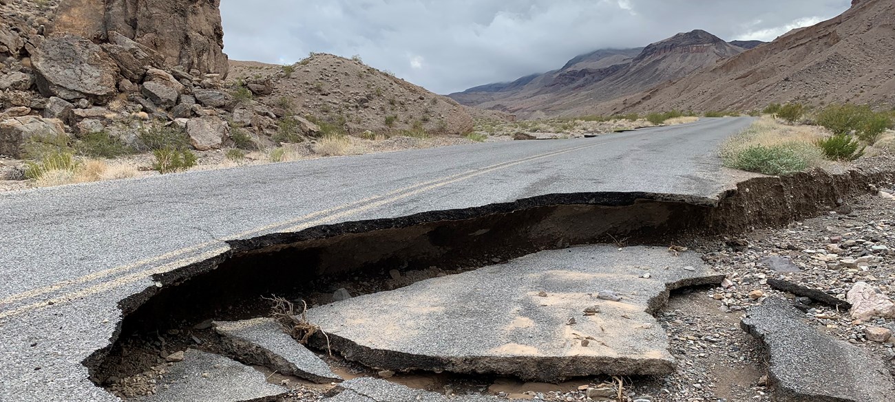 Pavement broken and undercut in a rocky mountain landscape.