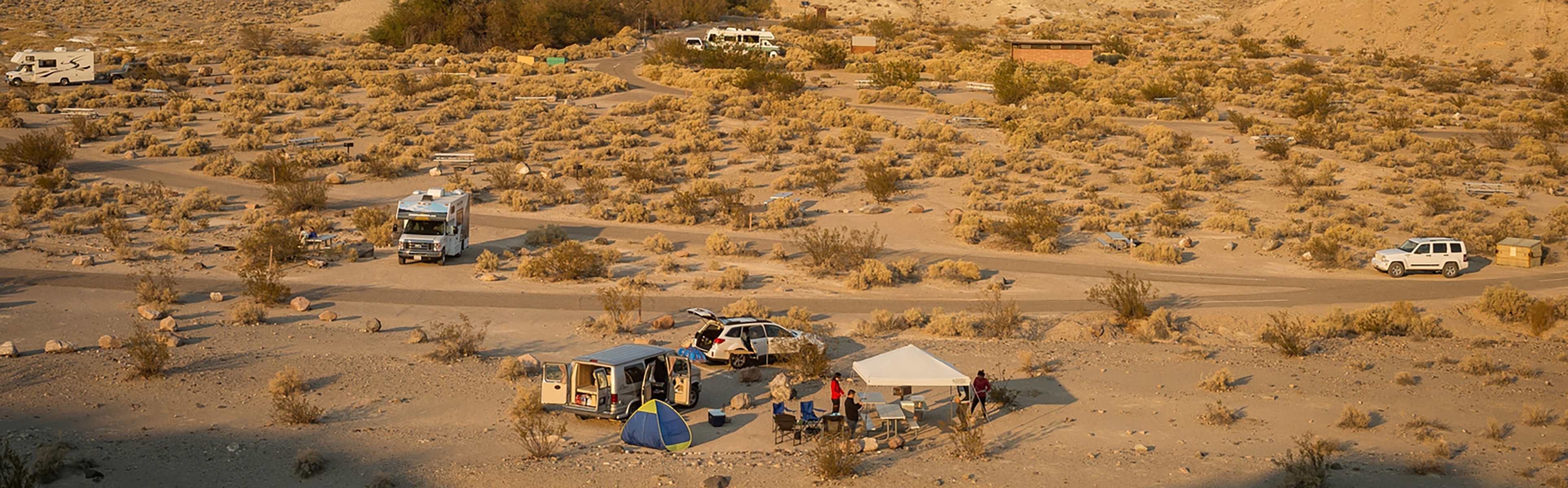 Desert landscape with occupied tent and RV camsite throughout the brush.