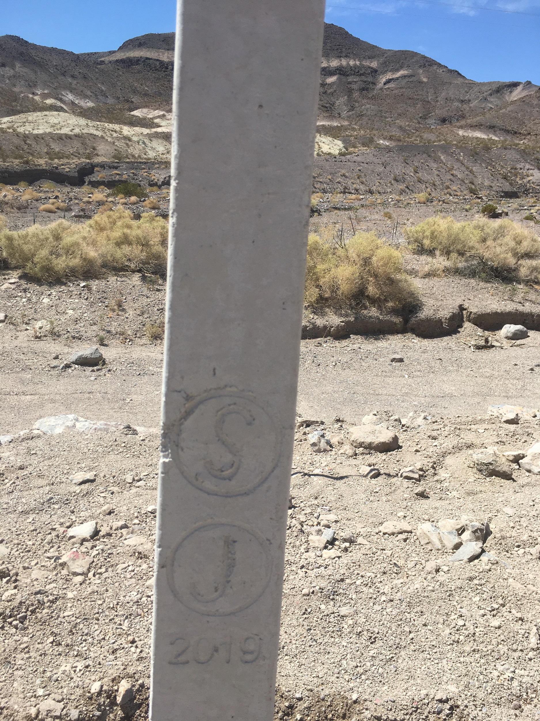 A close-up photo of a concrete fence post, stamped with a circle-S, circle-J, and 2019. 